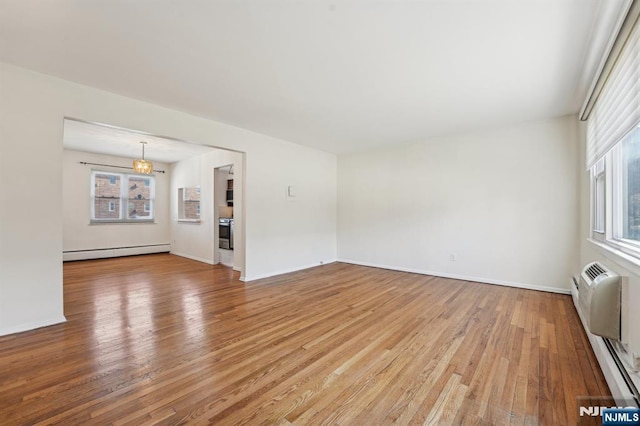 unfurnished living room with a baseboard heating unit, light wood-style flooring, and baseboards