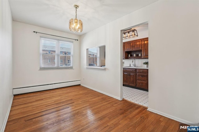 unfurnished dining area with light wood-style flooring, a baseboard heating unit, a sink, a chandelier, and baseboards