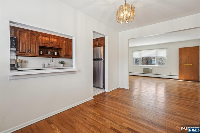 kitchen featuring a notable chandelier, a baseboard heating unit, a sink, light countertops, and freestanding refrigerator