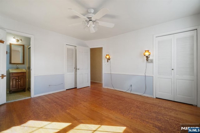 unfurnished bedroom with multiple closets, ensuite bathroom, a sink, wood finished floors, and baseboards