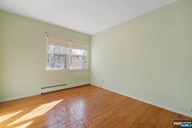 unfurnished room with baseboards, a baseboard heating unit, and wood finished floors