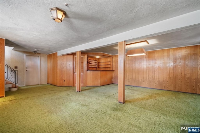 finished below grade area featuring carpet, wooden walls, a textured ceiling, and stairs