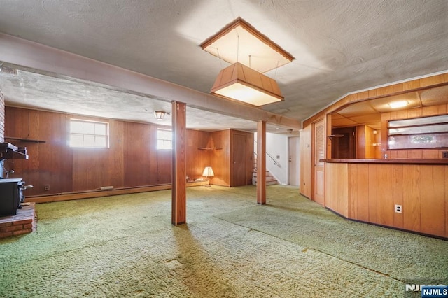 below grade area with a baseboard radiator, a wood stove, carpet, a textured ceiling, and wood walls