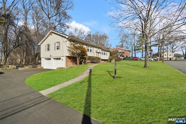 exterior space featuring a garage, brick siding, driveway, a chimney, and a front yard