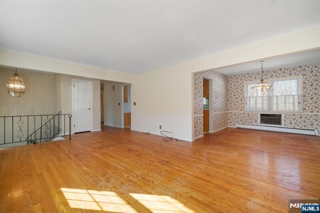 unfurnished living room featuring wallpapered walls, baseboard heating, and an inviting chandelier