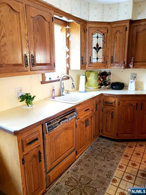 kitchen with dishwasher, light countertops, a sink, and brown cabinets