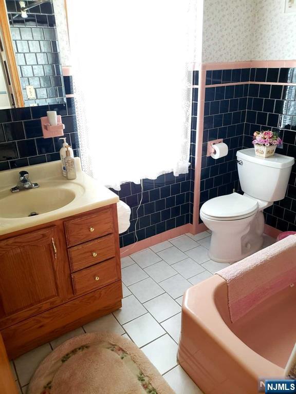 bathroom featuring wallpapered walls, toilet, tile patterned floors, vanity, and tile walls