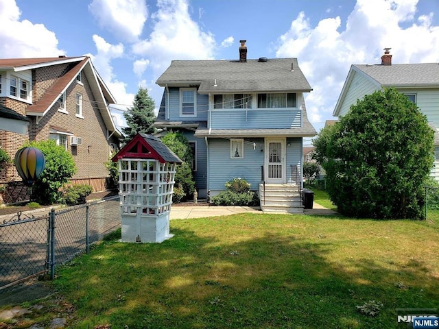 view of front of house with a front yard, a chimney, fence, and a balcony