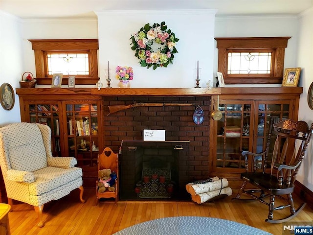 living area with ornamental molding, a brick fireplace, plenty of natural light, and wood finished floors