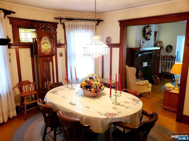 dining room with ornamental molding, a fireplace, wood finished floors, and wallpapered walls