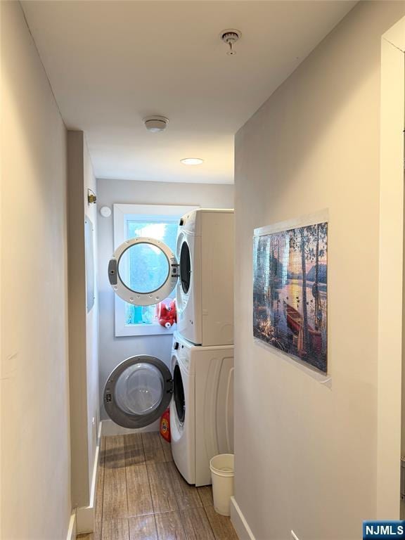 clothes washing area with stacked washer / drying machine, laundry area, baseboards, and wood finished floors