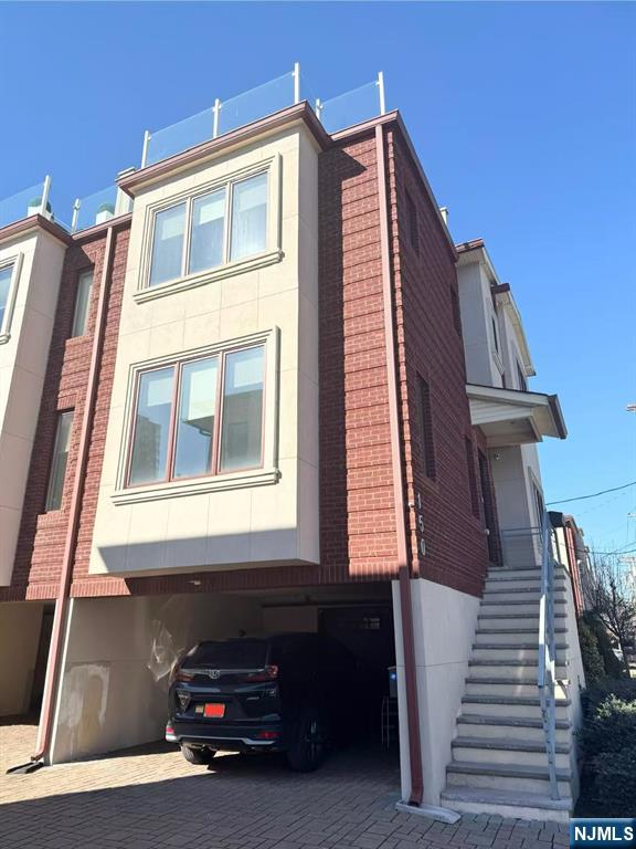 view of side of home featuring stucco siding, stairs, decorative driveway, and brick siding