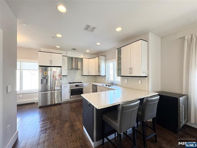 kitchen with visible vents, wall chimney exhaust hood, a peninsula, stainless steel appliances, and light countertops