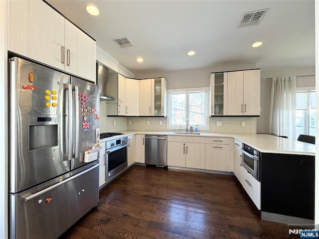 kitchen featuring wall chimney range hood, visible vents, appliances with stainless steel finishes, and a sink