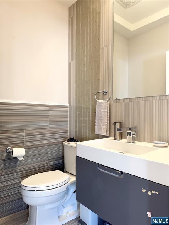 bathroom featuring a wainscoted wall, tile walls, toilet, and vanity