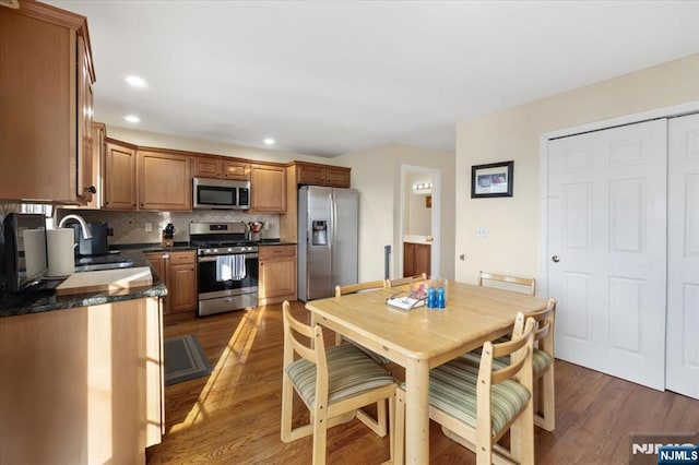 kitchen featuring wood finished floors, a sink, appliances with stainless steel finishes, decorative backsplash, and dark countertops