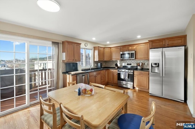 kitchen with stainless steel appliances, dark countertops, backsplash, and light wood finished floors