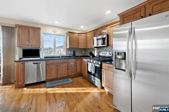 kitchen with decorative backsplash, dark countertops, appliances with stainless steel finishes, light wood-style floors, and a sink