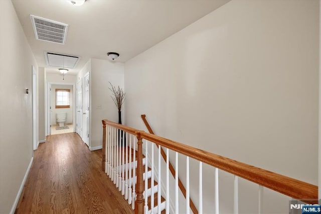 hall with wood finished floors, visible vents, an upstairs landing, baseboards, and attic access