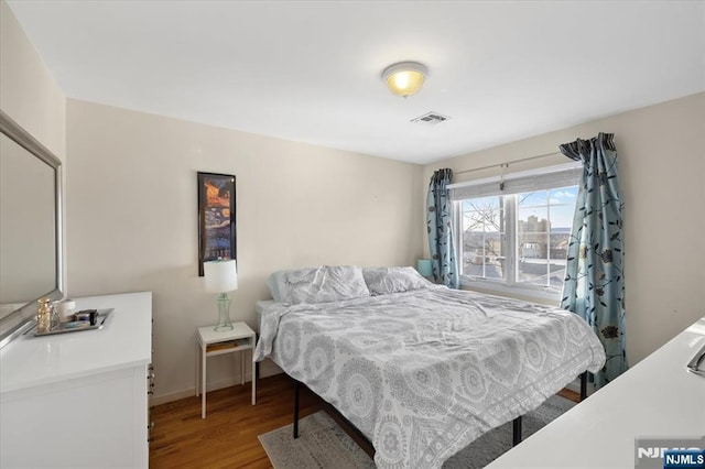 bedroom with wood finished floors, visible vents, and baseboards