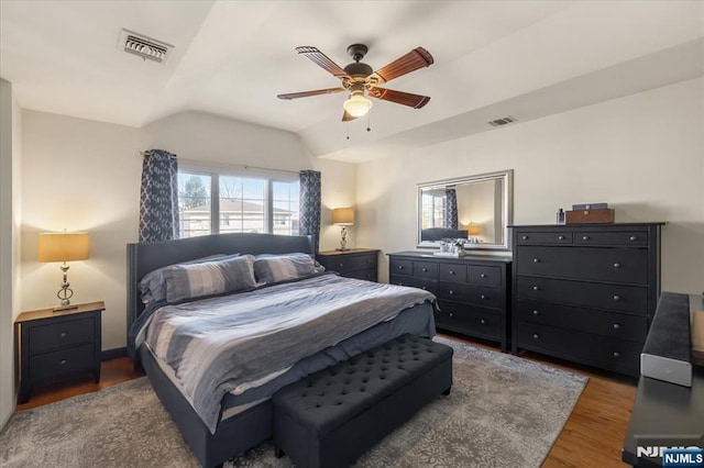 bedroom featuring a ceiling fan, visible vents, vaulted ceiling, and wood finished floors