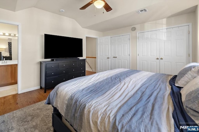 bedroom featuring baseboards, visible vents, wood finished floors, vaulted ceiling, and two closets