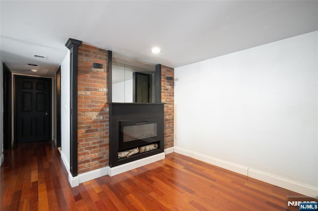 unfurnished living room with visible vents, baseboards, wood finished floors, and a glass covered fireplace