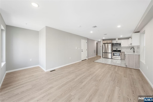 kitchen featuring tasteful backsplash, stainless steel appliances, light countertops, light wood-type flooring, and a sink