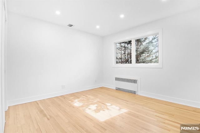 unfurnished room with baseboards, visible vents, radiator heating unit, and wood finished floors