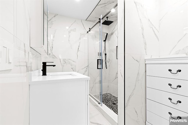 bathroom with a marble finish shower, tile walls, and vanity