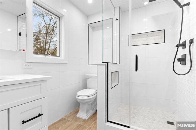 bathroom with tile walls, toilet, a shower stall, vanity, and wood finished floors