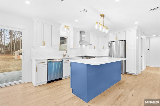 kitchen featuring visible vents, white cabinets, a kitchen island, appliances with stainless steel finishes, and wall chimney range hood