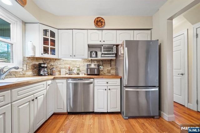 kitchen featuring light wood-style flooring, stainless steel appliances, a sink, decorative backsplash, and glass insert cabinets