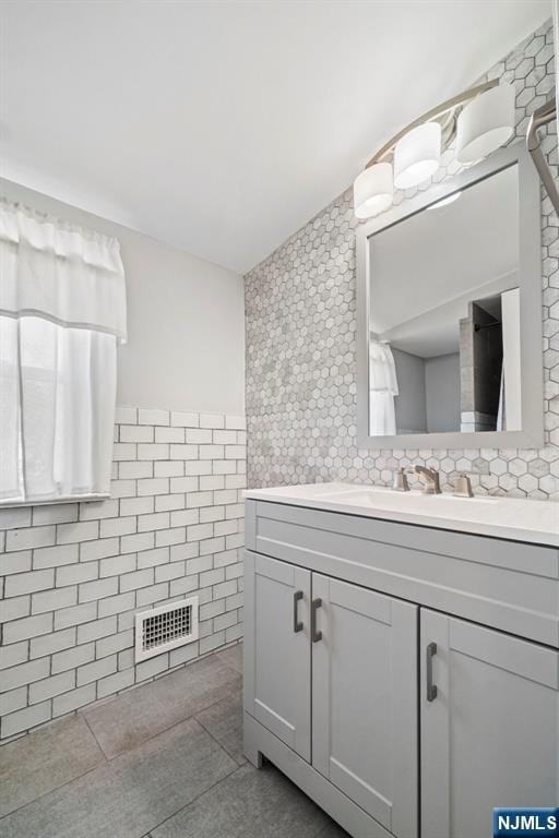 bathroom featuring visible vents, wainscoting, tile patterned flooring, vanity, and tile walls