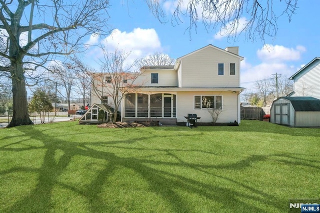 rear view of property featuring a yard, a sunroom, an outdoor structure, and a storage unit