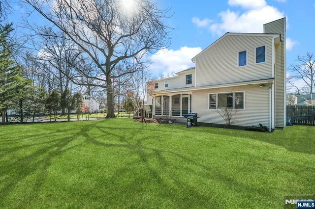 rear view of house featuring a sunroom, a yard, a chimney, and fence