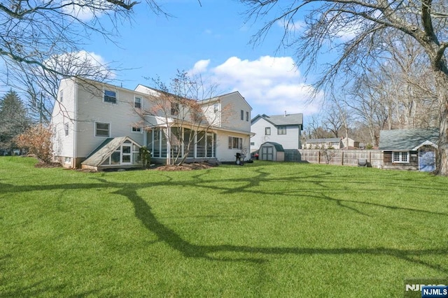 rear view of house featuring a yard, a storage shed, a sunroom, fence, and an outdoor structure