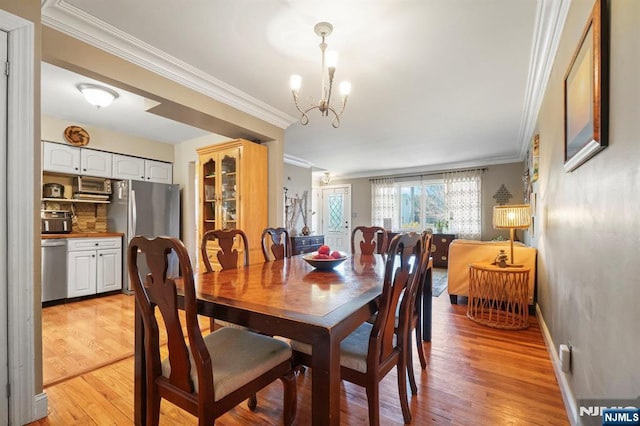 dining room featuring crown molding, light wood-style flooring, baseboards, and an inviting chandelier