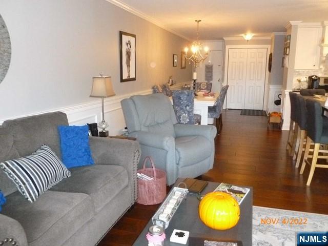 living room with an inviting chandelier, dark wood finished floors, crown molding, and wainscoting