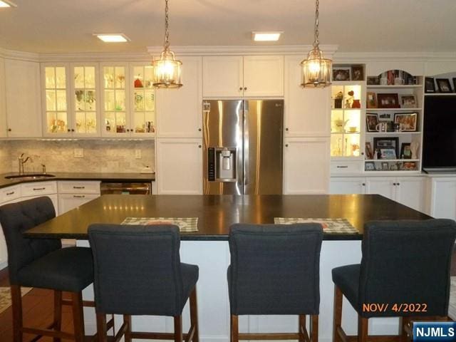 kitchen featuring dark countertops, white cabinets, a sink, and stainless steel fridge with ice dispenser