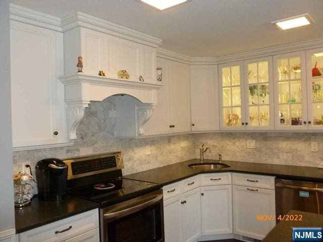 kitchen featuring appliances with stainless steel finishes, dark countertops, white cabinetry, and a sink