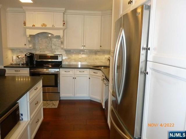 kitchen featuring dark countertops, appliances with stainless steel finishes, dark wood-type flooring, white cabinetry, and a sink