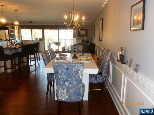 dining space featuring a notable chandelier, a decorative wall, dark wood-style flooring, wainscoting, and crown molding