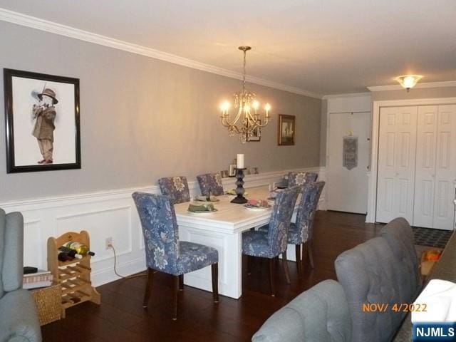 dining area featuring crown molding, a notable chandelier, a decorative wall, wainscoting, and wood finished floors