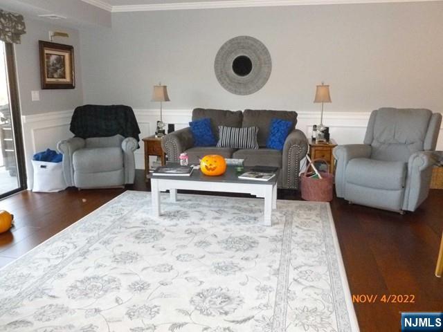 living room with ornamental molding, a decorative wall, wood finished floors, and wainscoting