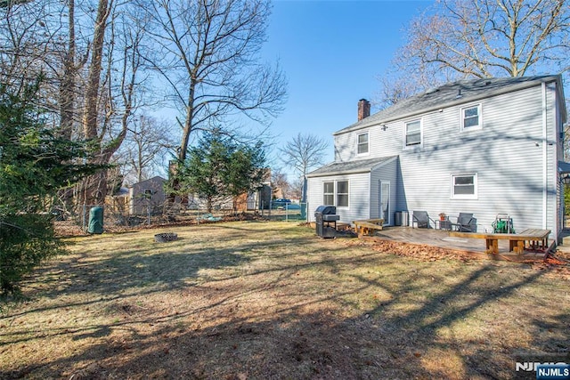 rear view of house featuring a chimney, fence, and a lawn