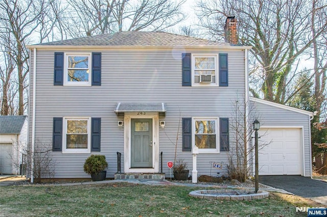 colonial home featuring roof with shingles, a chimney, a front yard, a garage, and driveway