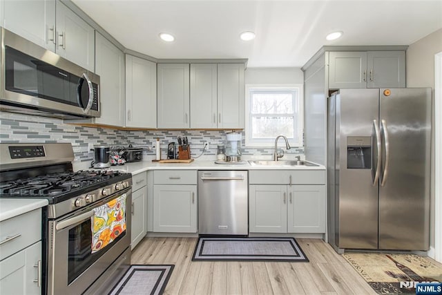 kitchen with appliances with stainless steel finishes, gray cabinets, a sink, and light wood finished floors