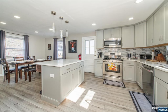 kitchen with stainless steel appliances, tasteful backsplash, gray cabinets, light countertops, and light wood-style floors