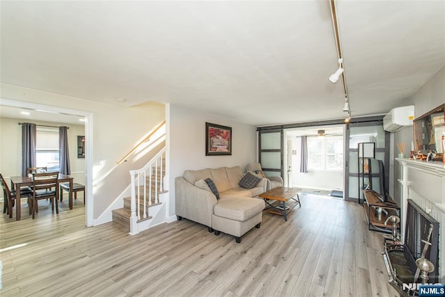 living area featuring a fireplace with raised hearth, a wall unit AC, stairway, light wood finished floors, and rail lighting